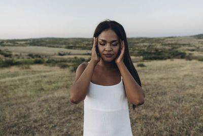 Woman with eyes closed rubbing head in meadow