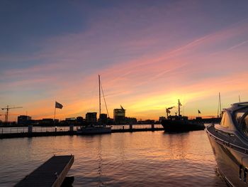 Sailboats moored at harbor against sky during sunset