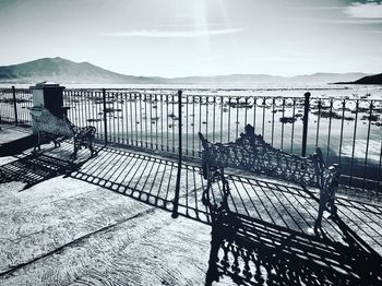 Empty bench on railing by sea against sky