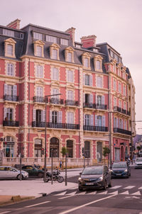 Cars on road by buildings in city against sky
