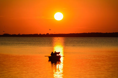 Silhouette men in sea against sky during sunset