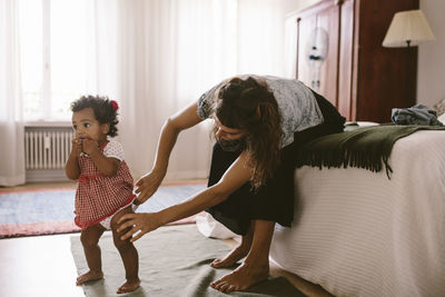 Mid adult woman adjusting diaper of daughter while sitting on bed at home