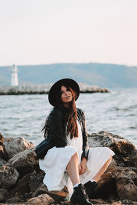 Young woman standing on rock by sea against sky