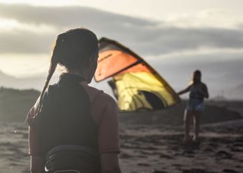 Friends with kite standing at beach against sky during sunset