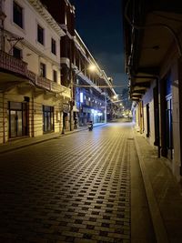 Empty footpath amidst illuminated buildings in city at night