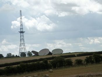 Electricity pylon on field against cloudy sky