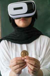 Woman wearing virtual reality simulator while holding bitcoin at home