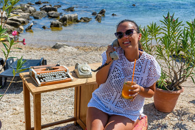 Young woman using telephone and having drink at beach