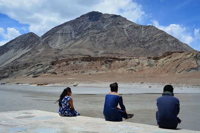 Rear view of women sitting on desert against mountain