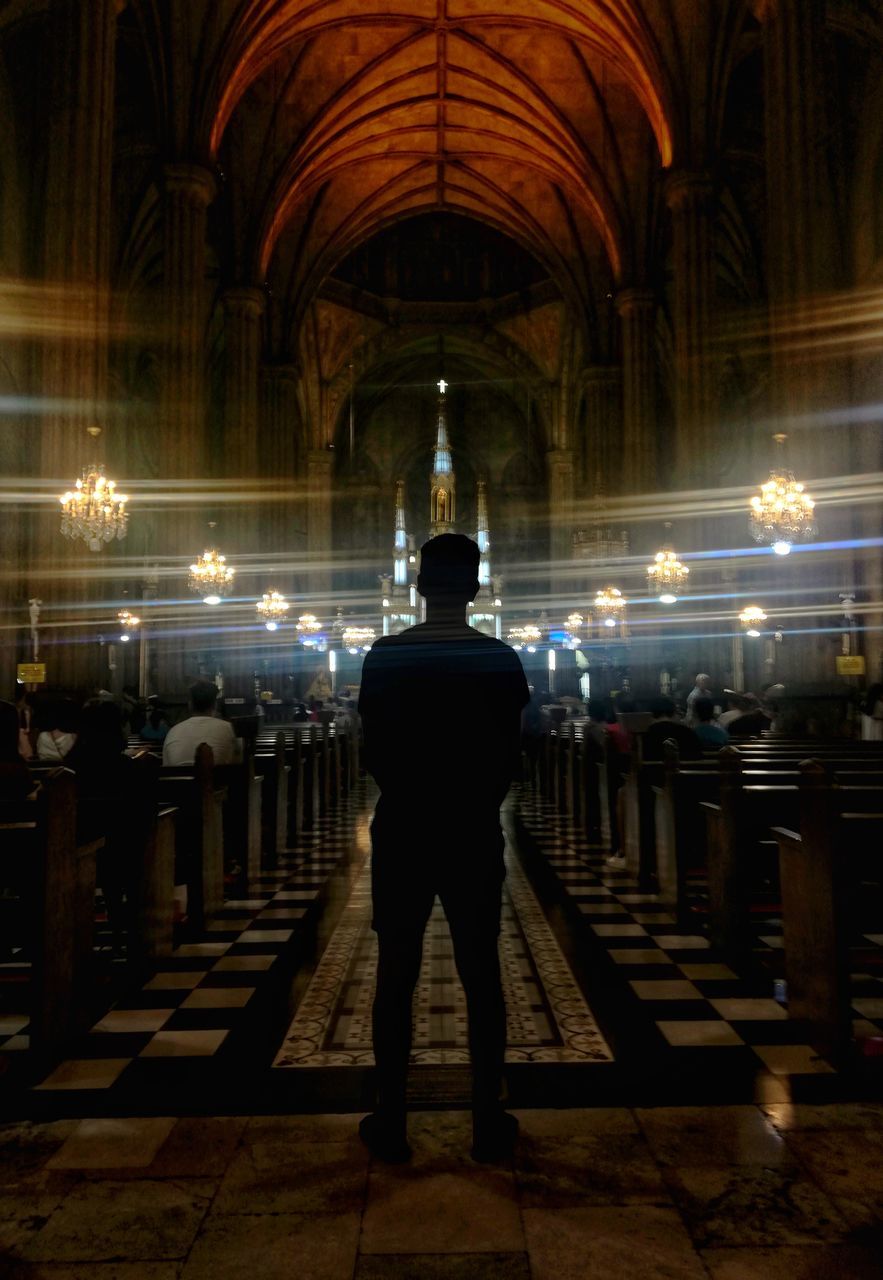 FULL LENGTH REAR VIEW OF MAN STANDING AT ILLUMINATED BUILDING