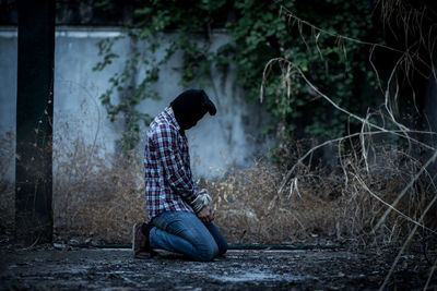 Side view of young man sitting on land in forest