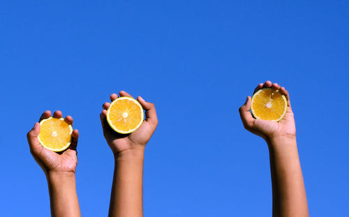 Cropped hands holding lemon slices against clear blue sky