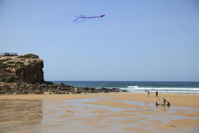 Kite flying over people at beach against clear sky