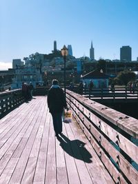 Rear view of man walking on footbridge against cityscape