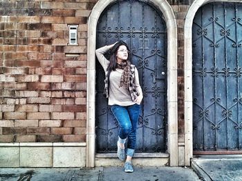 Portrait of young woman standing against brick wall