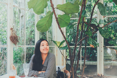 Portrait of young woman sitting on plant against trees