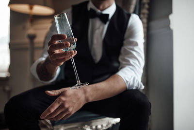 Midsection of groom holding champagne flute sitting outdoors