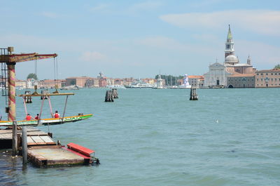 Sailboats in sea by buildings in city against sky
