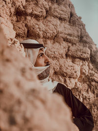 Close-up of man looking away while standing by rock formation