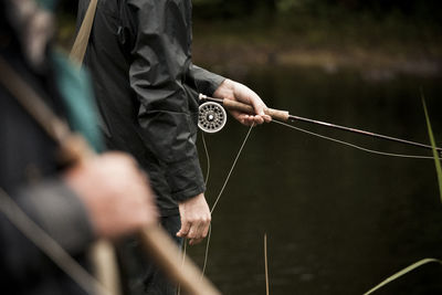 Midsection of man holding fly fishing rod