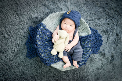 High angle view of cute baby boy lying down in basket with stuffed toy on rug