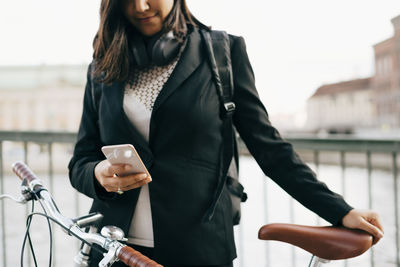 Young woman holding bicycle while standing on bridge