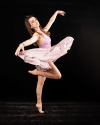 Full length of young woman dancing against black background