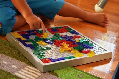 Low section of boy playing board game while sitting on hardwood floor