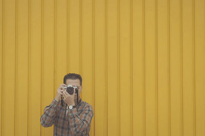 Man photographing against yellow wall