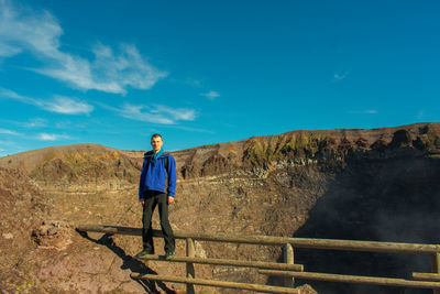 Portrait of young man standing on railing against blue sky