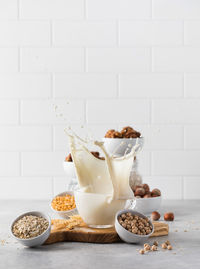 A splash of vegetable milk in a mug against the background of bowls with nuts, oatmeal and legumes.