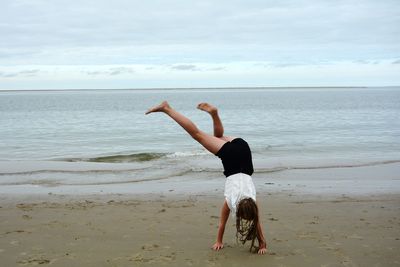 Girl doing handstand on shore at beach against sky