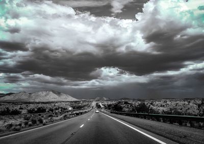 Empty road along landscape against cloudy sky