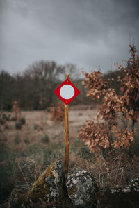 Road sign by trees on field against sky