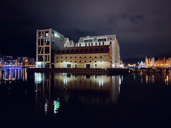 Illuminated buildings by river against sky at night