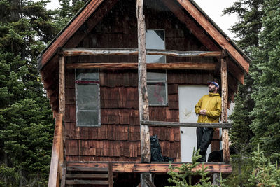 Low angle of male hiker leaning on abandoned wooden cabin in forest while relaxing during trekking in british columbia and looking away