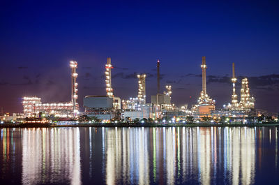 Illuminated factory by river against sky at night oil refinery