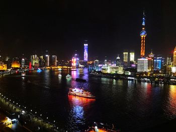 Illuminated buildings by river against sky at night