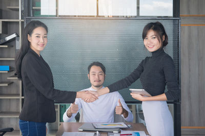 Side view portrait of businesswoman shaking hands with male coworker sitting in office