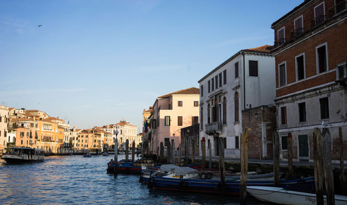 Boats moored on canal in city against clear sky