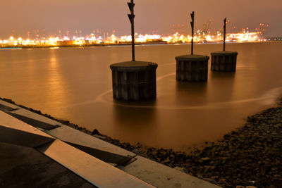 Illuminated lamp post by sea against sky at night