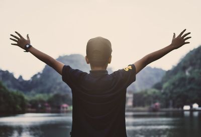 Rear view of man with arms outstretched standing by lake