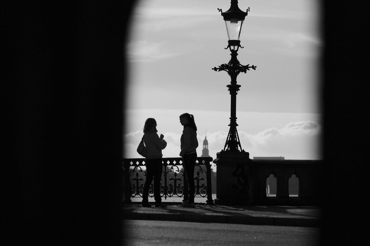 SILHOUETTE PEOPLE ON STREET LIGHT AGAINST BUILDING