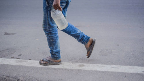 Low section of man carrying water in plastic bottle while walking on road