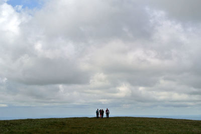Hikers on hill against cloudy sky
