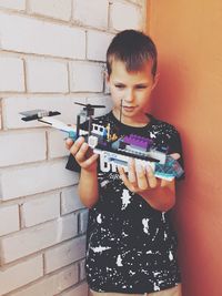 Smiling boy holding toy while standing by wall