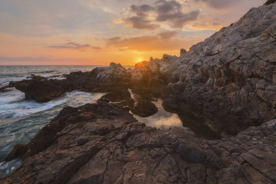 Rocks on beach against sky during sunset