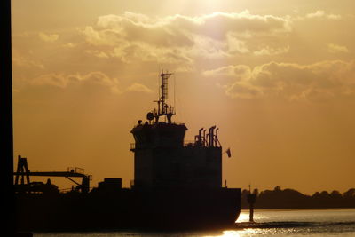 Silhouette cranes at commercial dock against sky during sunset