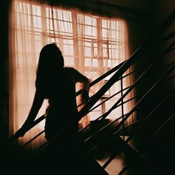 Silhouette woman standing by window at home