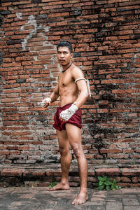 Full length of shirtless man standing against brick wall